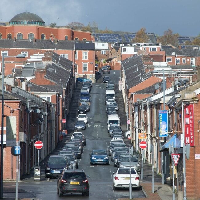 Red brick terraced housing, shops and businesses with a large domed mosque in the background. Photograph of Charlotte Street in Blackburn.