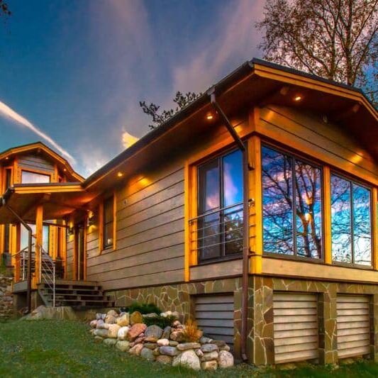 A wooden cottage with a green lawn. Cottage with panoramic windows. Glazing of cottages. Large windows in the house.