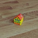 A small wooden model of a house sits on a laminate floor.